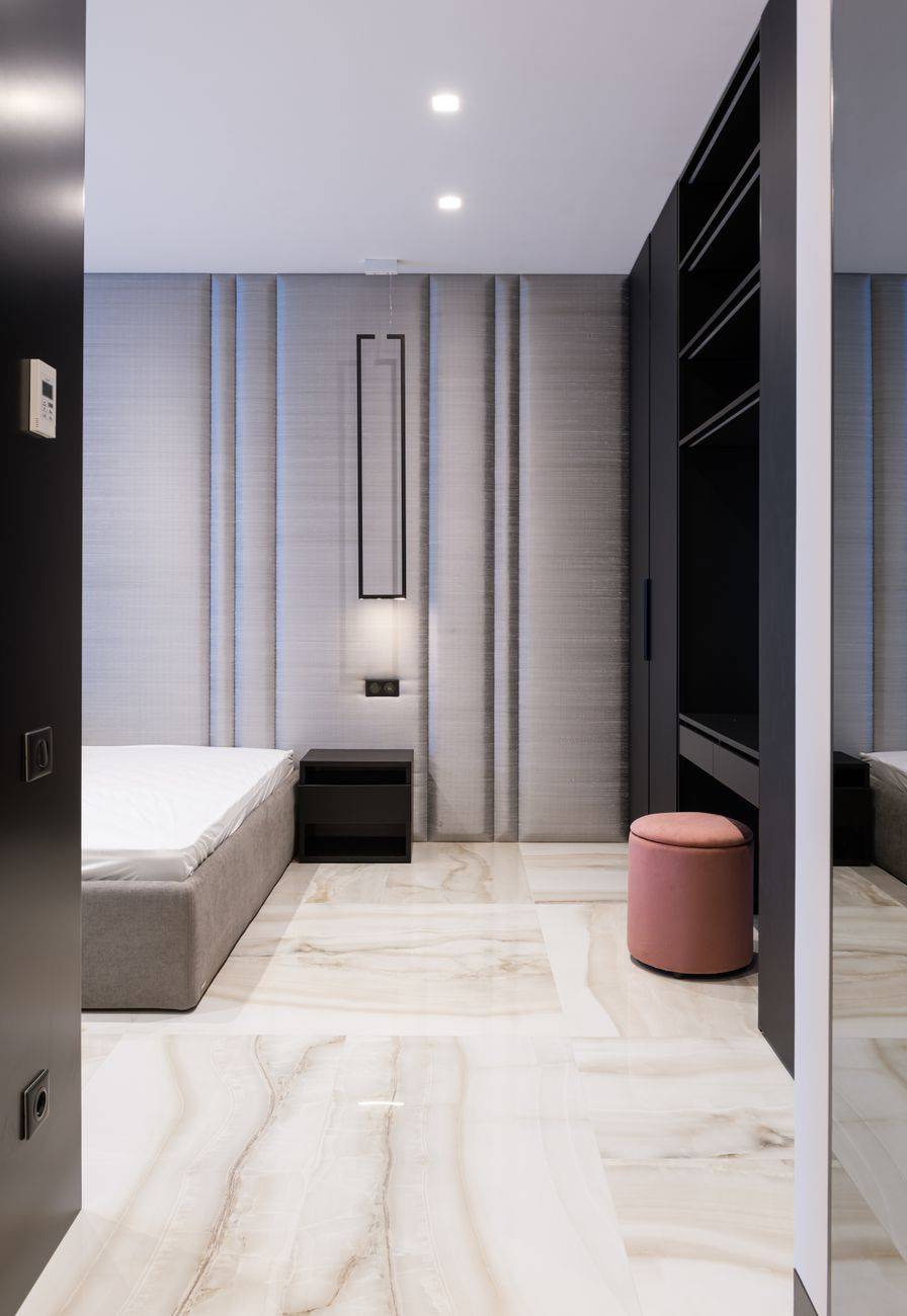 Interior of contemporary house with mattress on bed near table and pouf near cabinet with shelves