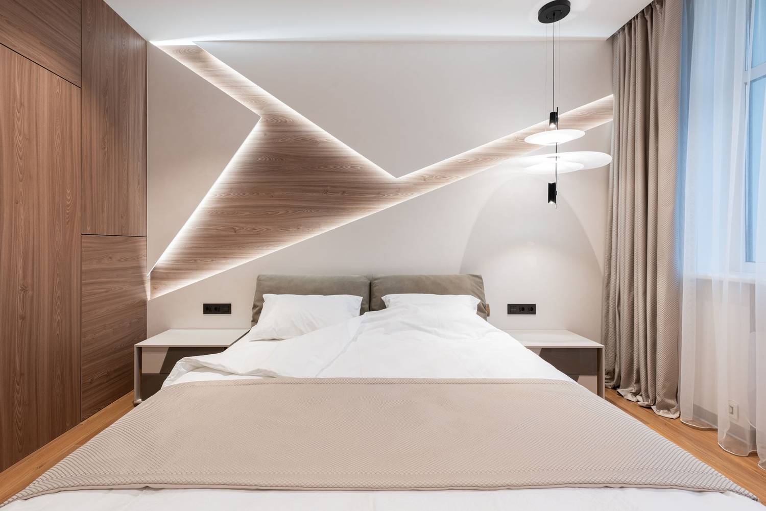 Light modern hotel room interior with soft white bed on wooden floor near window with curtains
