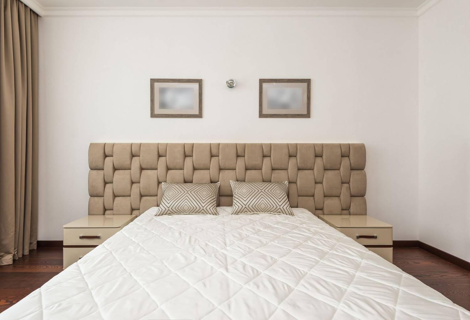 Elegant beige bedroom featuring a quilted headboard, plush pillows, and minimalistic decor.