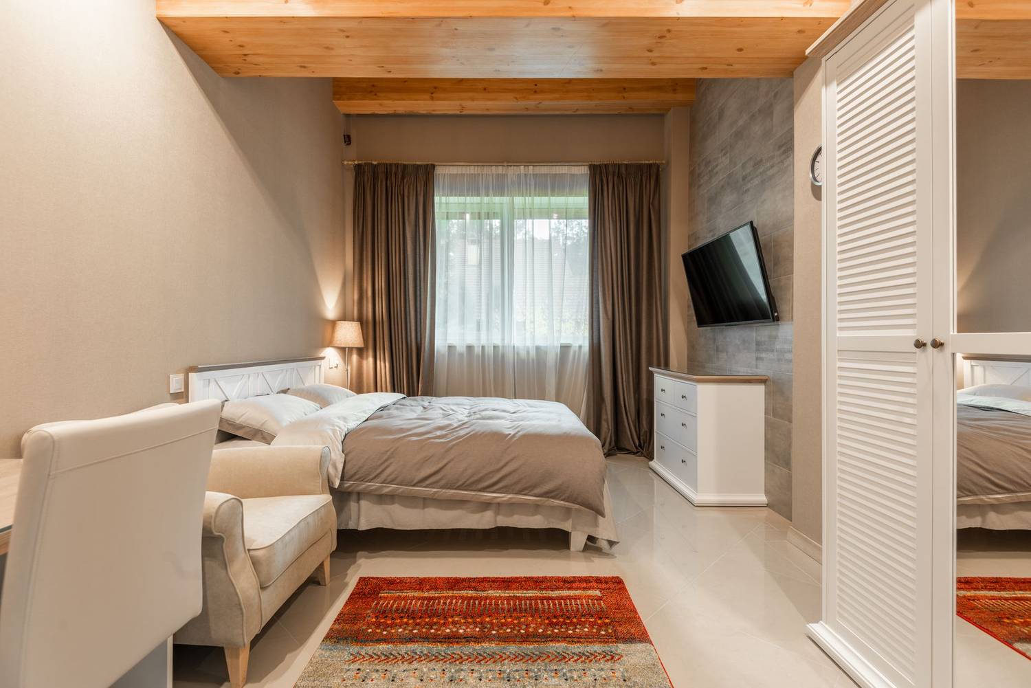Interior of contemporary light bedroom with soft bed against TV and white dresser near window with curtains