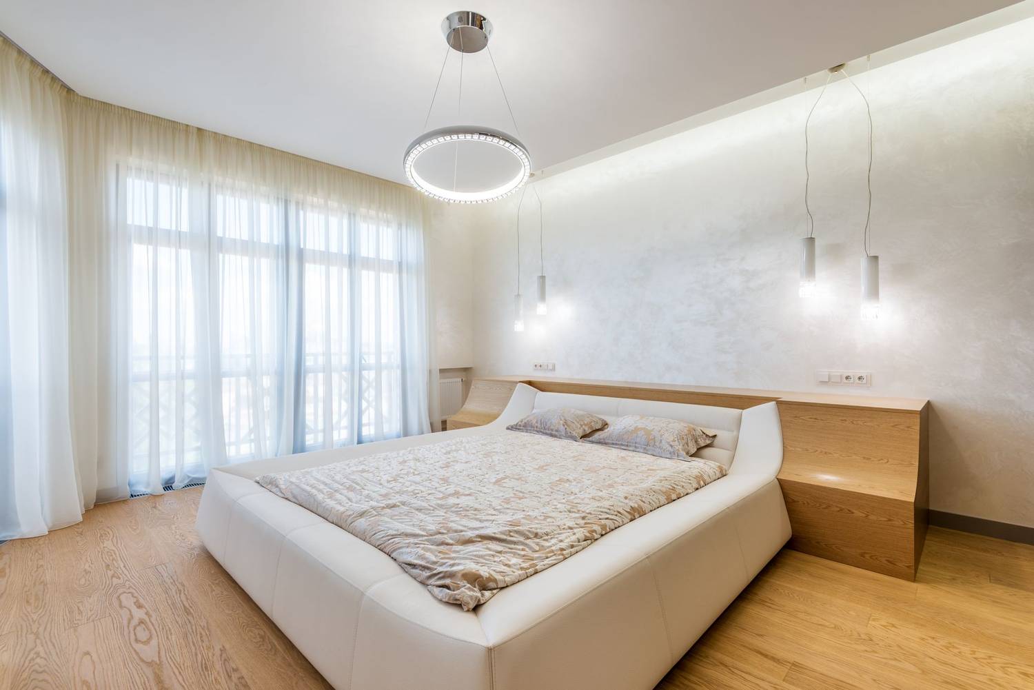 Interior design of minimalistic modern bedroom furnished with comfortable bed and bedside nightstands decorated with ring shaped chandelier 