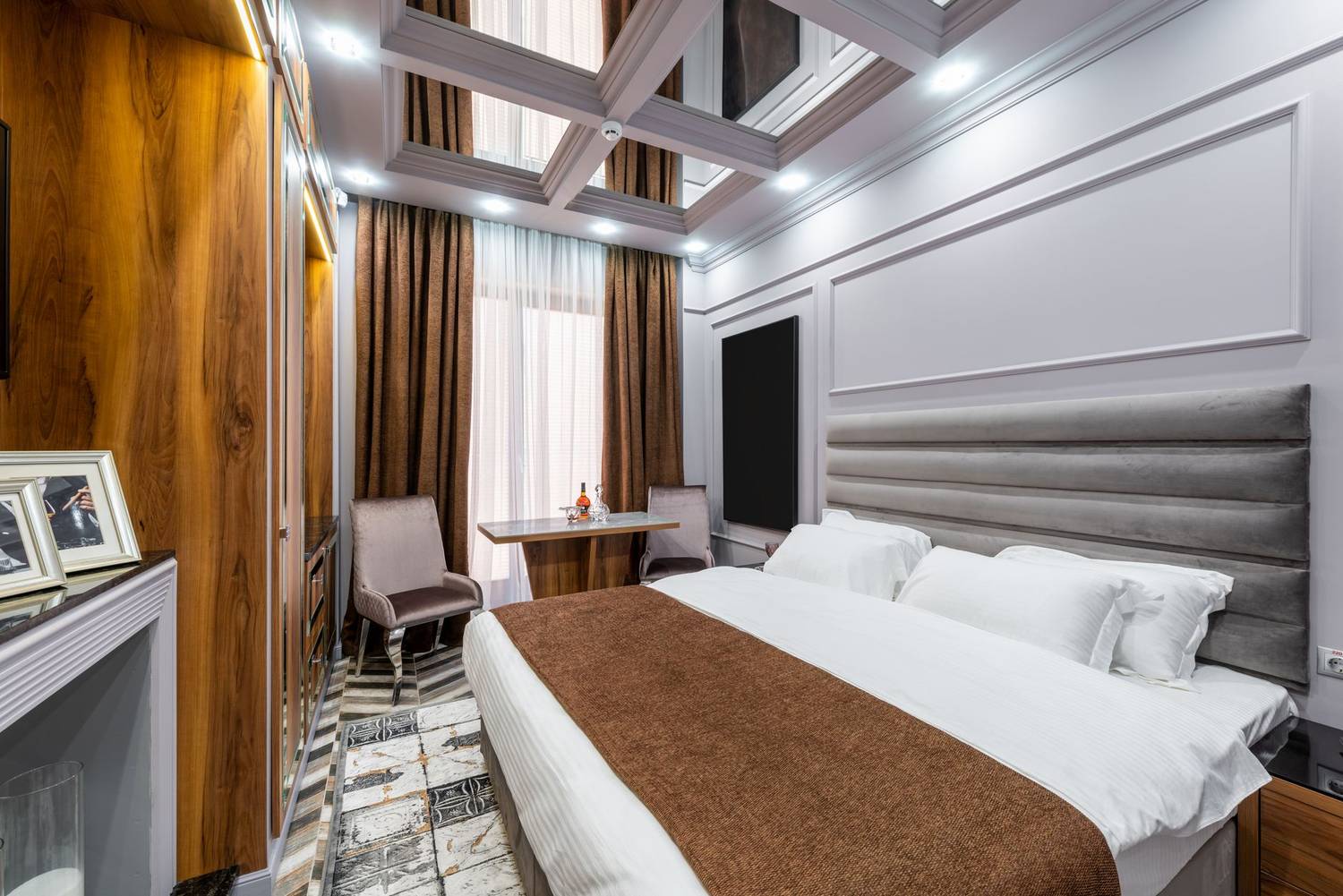 Contemporary bedroom interior with pillows on bed against photos and table illuminated by glowing lamps