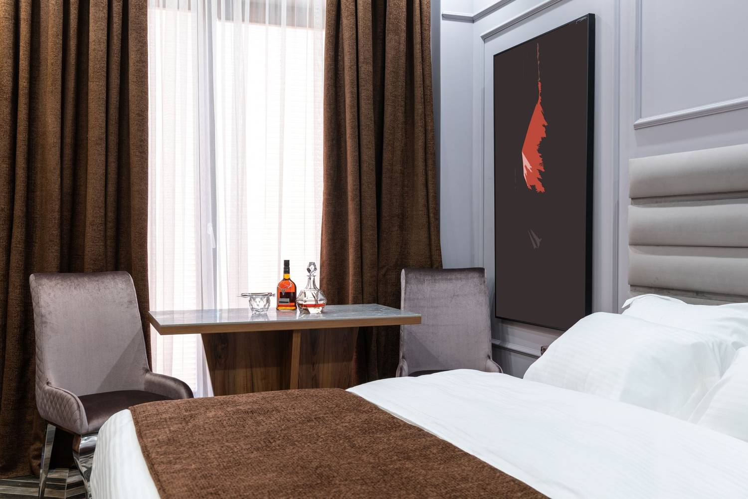 Soft bed against armchairs and table with carafe and bottle of liquor in light hotel room