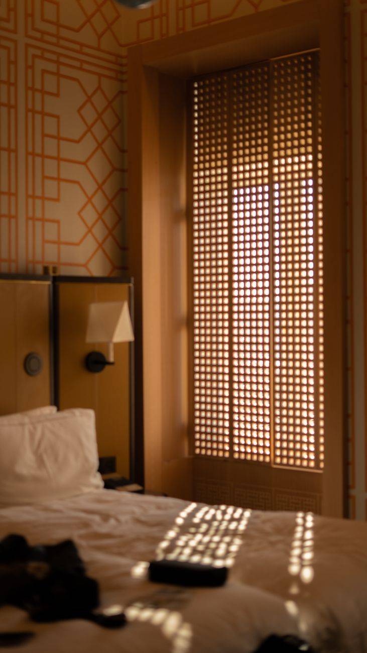 Warm and inviting bedroom with sunlight casting patterns through shutters, creating a tranquil atmosphere.