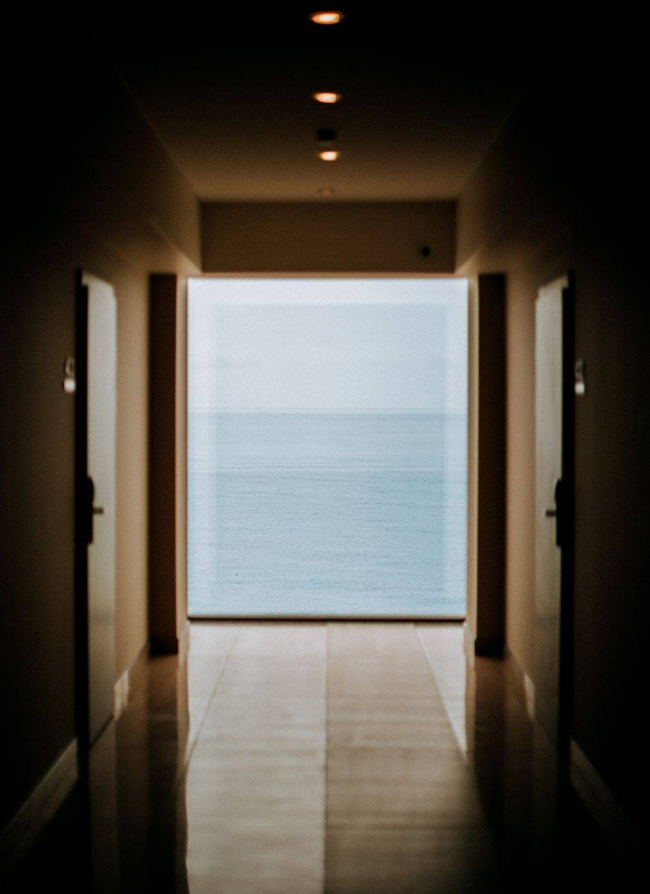 Contemporary hotel hallway leading to a serene ocean view through a large glass panel.