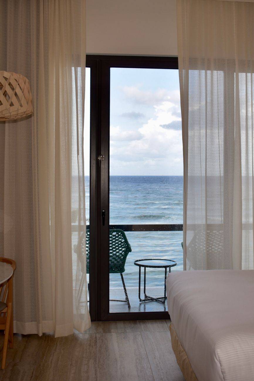Inviting hotel room with a balcony providing a stunning ocean view through sheer curtains.
