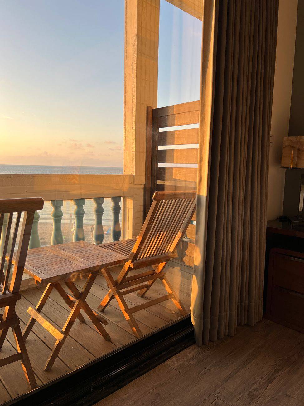 A tranquil sunset view from a wooden balcony overlooking the ocean.