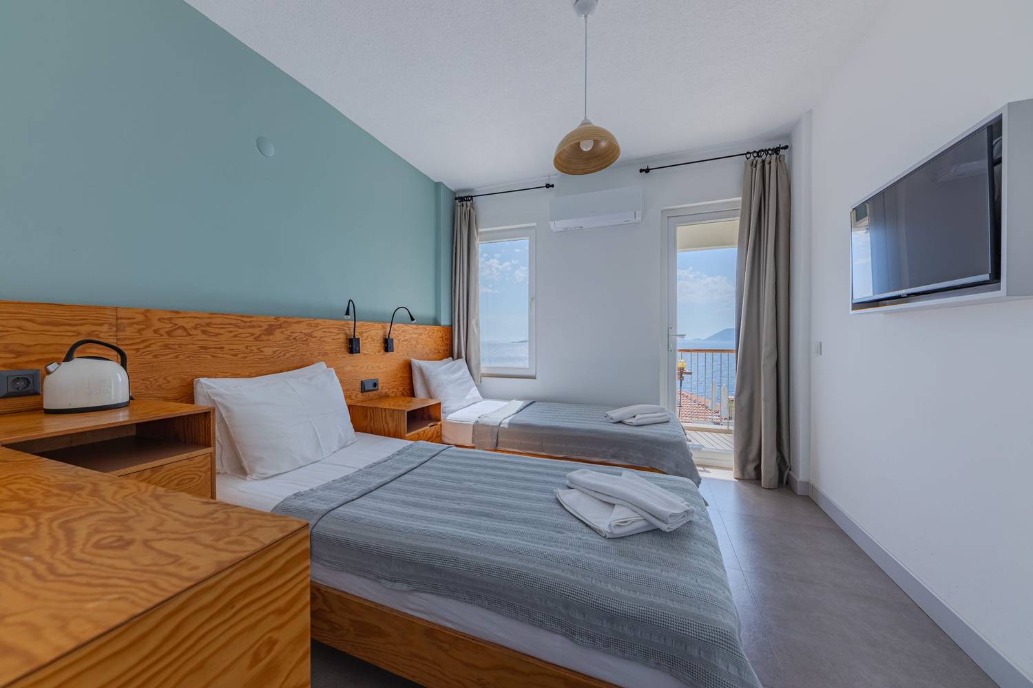 Bright hotel room featuring twin beds, modern decor, and a stunning sea view.