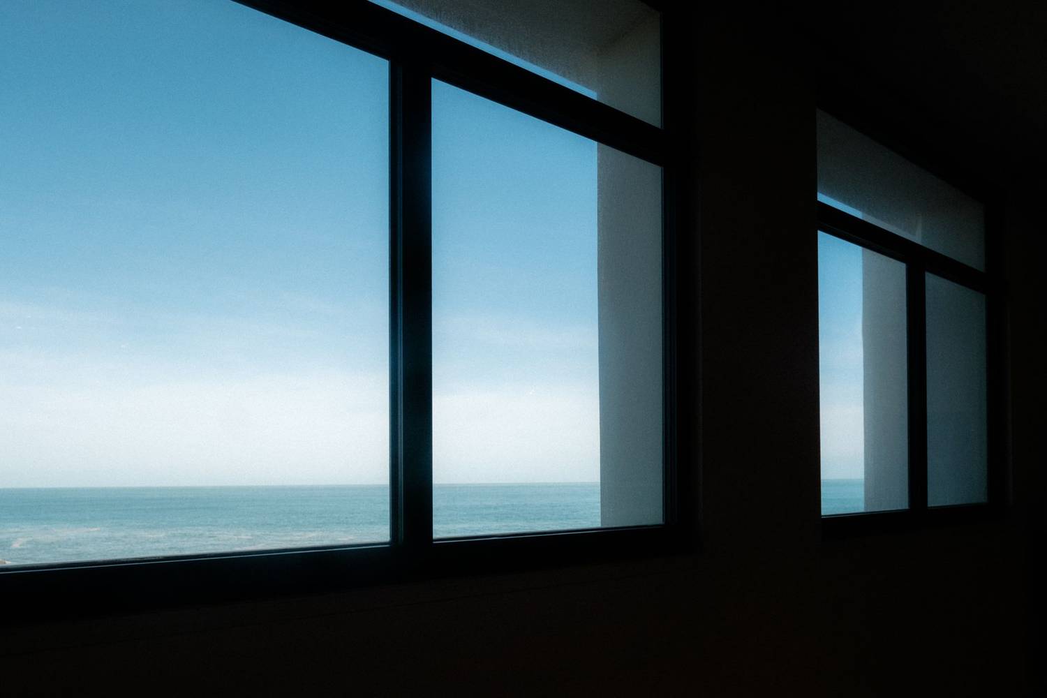 A tranquil ocean scene captured through large windows, showcasing blue sky and sea.