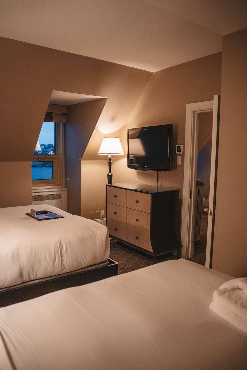 A warmly lit hotel room in Québec, Canada with two beds and TV.