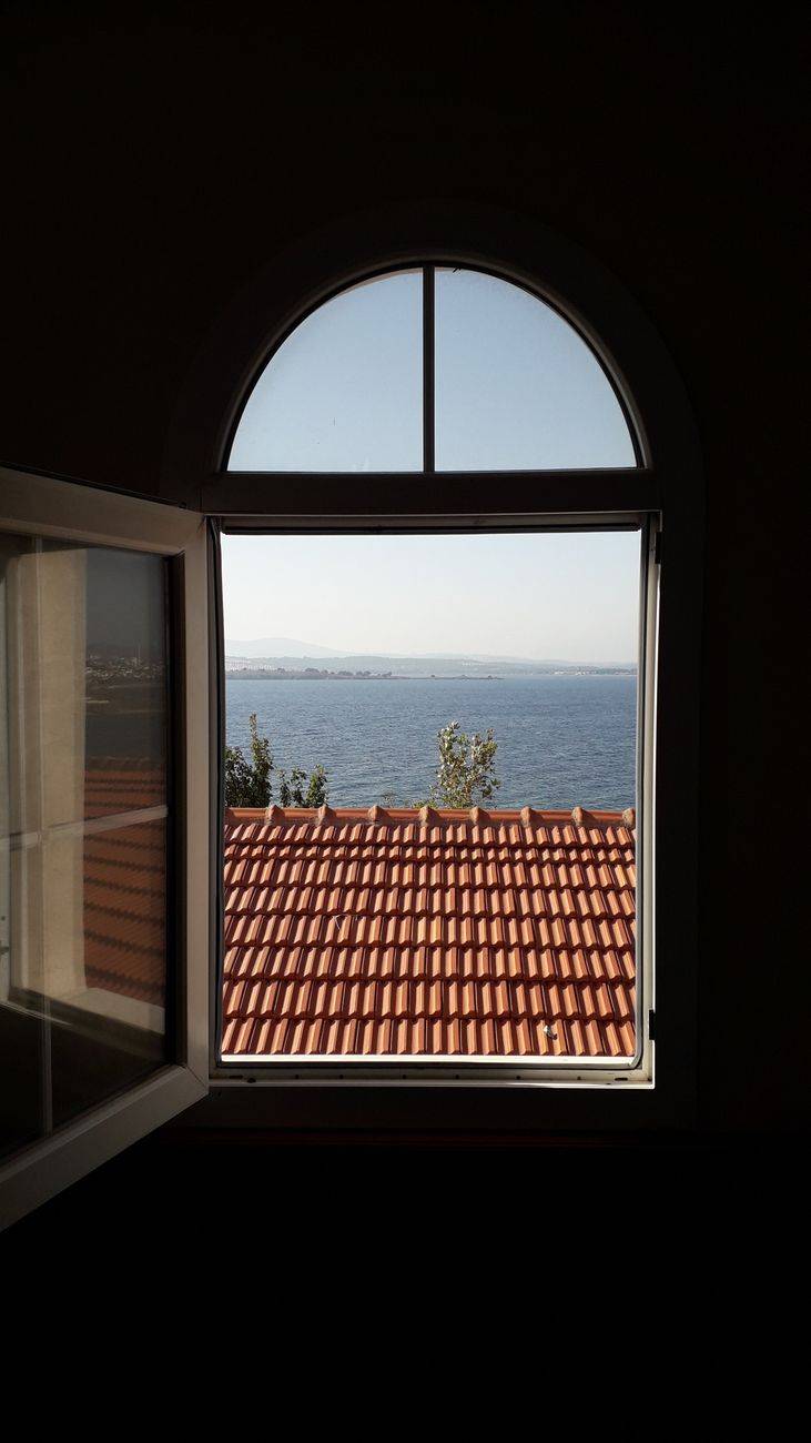 View of the ocean framed by an arched window overlooking a tiled roof in Izmir, Turkey.