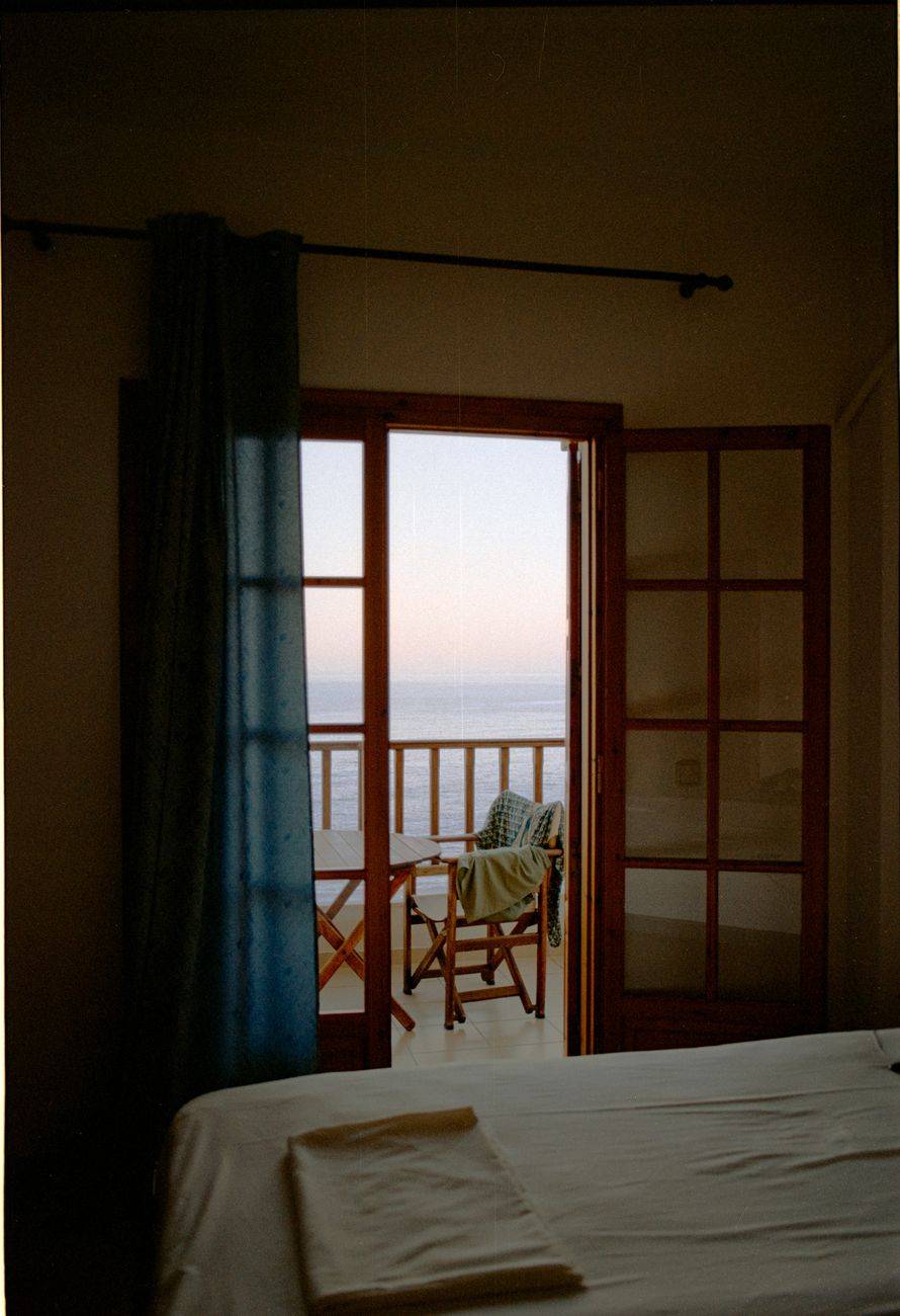 Serene bedroom with open balcony doors overlooking the ocean at sunset for relaxation.