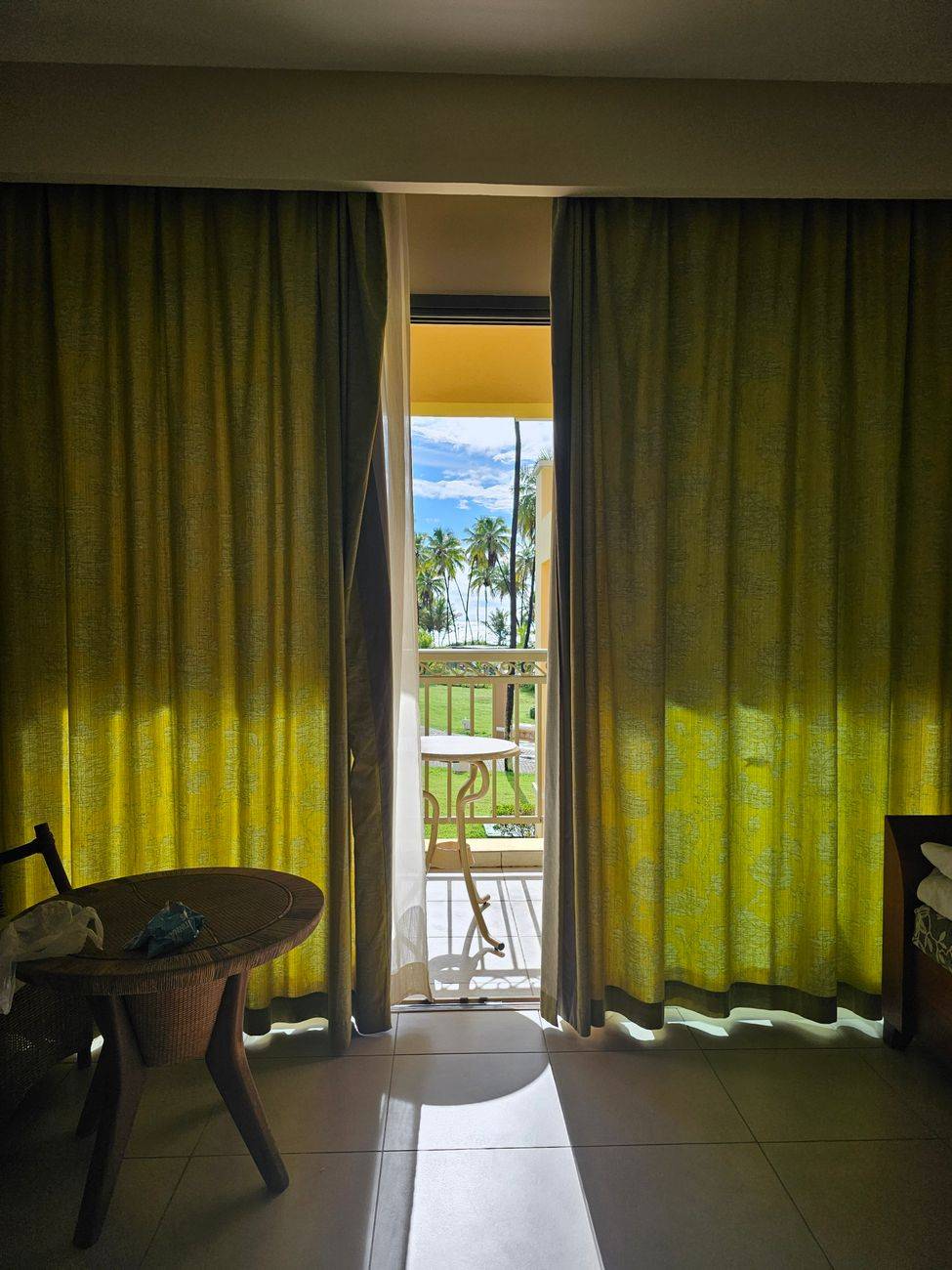 Bright room with curtains open to a balcony and lush palm trees.