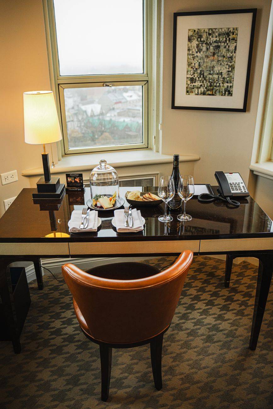 A luxurious hotel room with a dining setup near a window overlooking Québec City, offering a sophisticated ambiance.