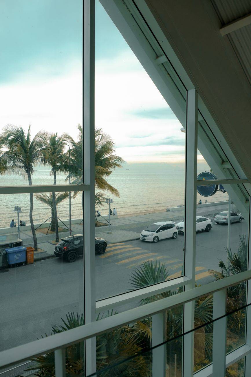 View of beachfront with palm trees and cars from a hotel window, perfect travel destination.