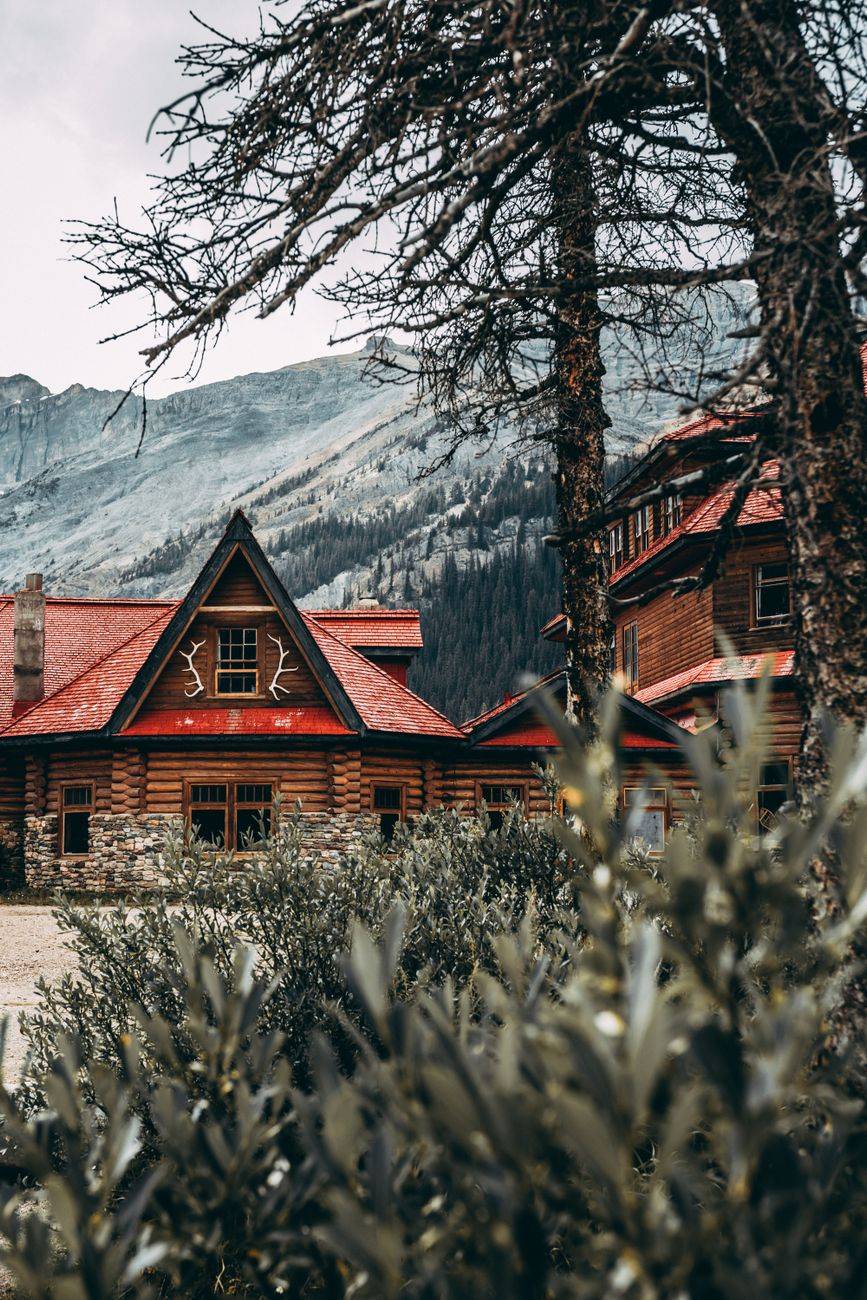 Charming mountain lodge with red roof nestled in a forested valley with scenic mountain views.