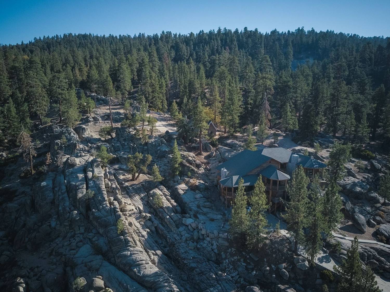 A scenic aerial shot of a forested area with a lodge nestled among rocky terrains, captured in daylight.