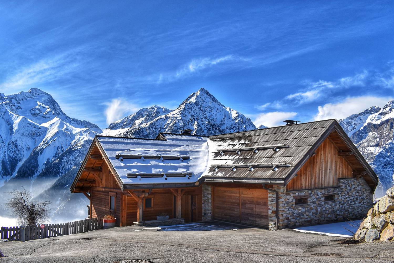 Beautiful wooden cabin surrounded by snow-covered mountains under a bright blue sky.
