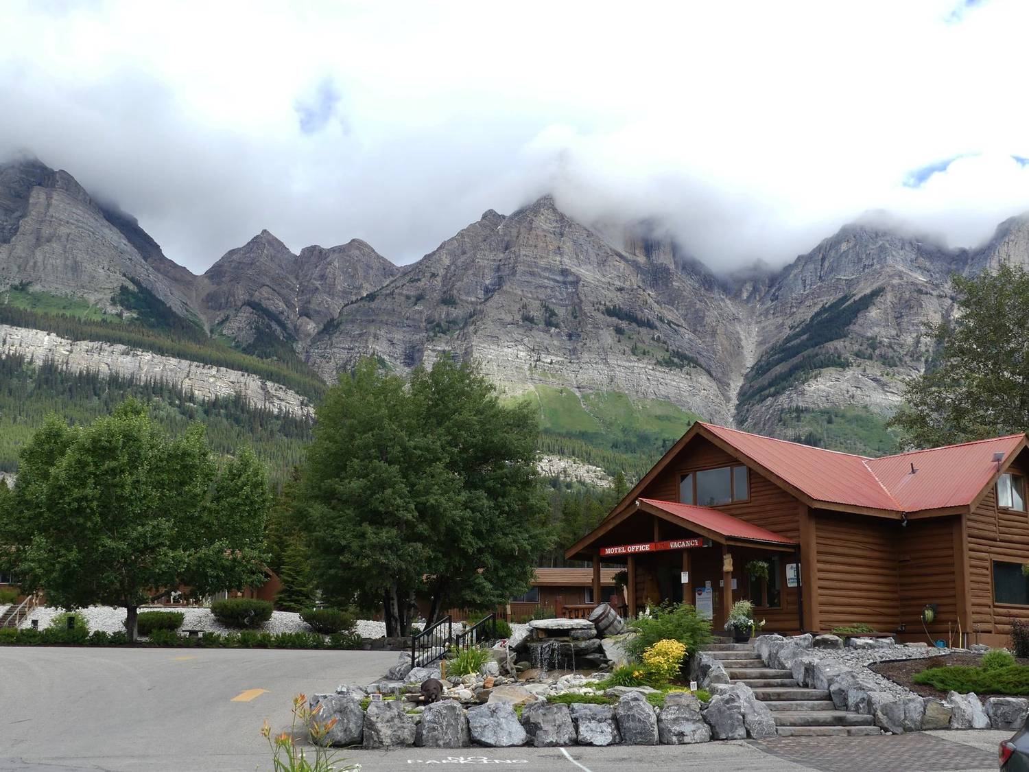 Charming mountain lodge set against towering rocky peaks under cloudy skies.