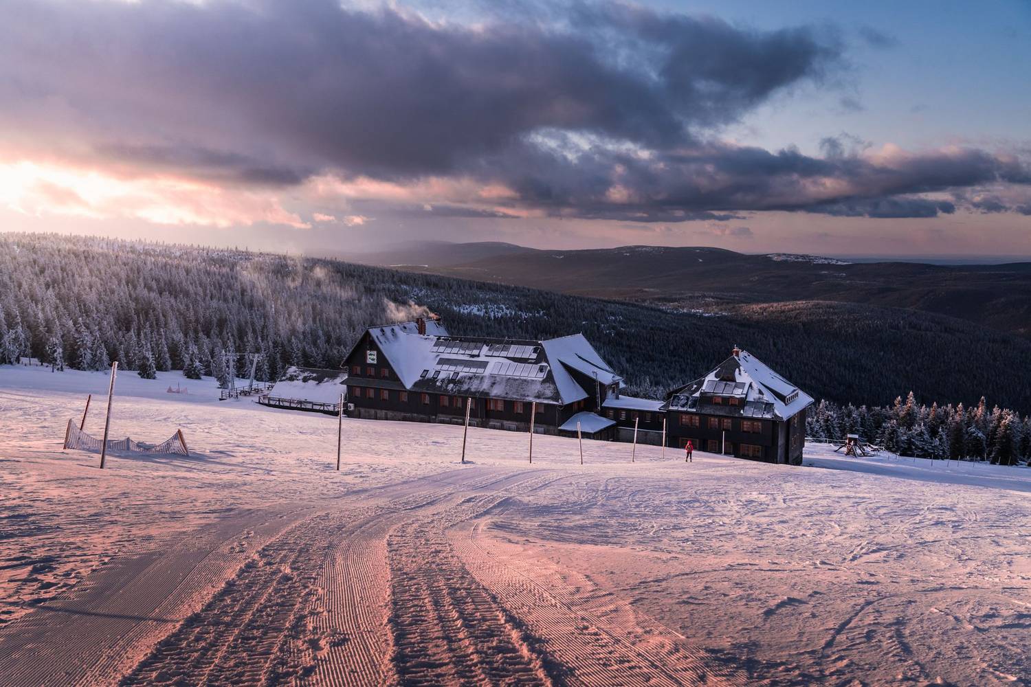 A scenic view of a snow-covered mountain lodge surrounded by winter forests at sunrise.