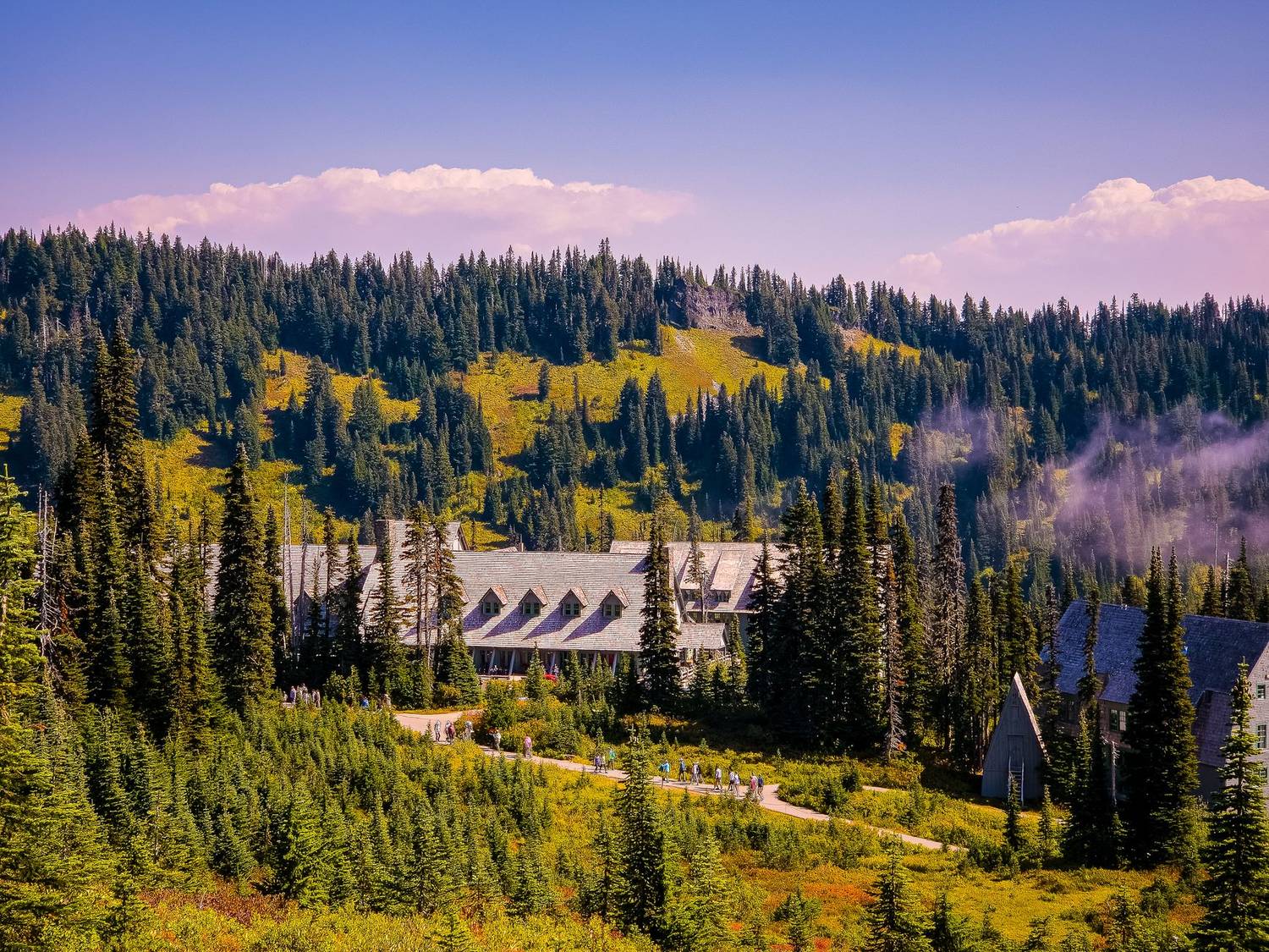 Mountain lodge nestled amidst lush evergreen forest, under vibrant blue sky.