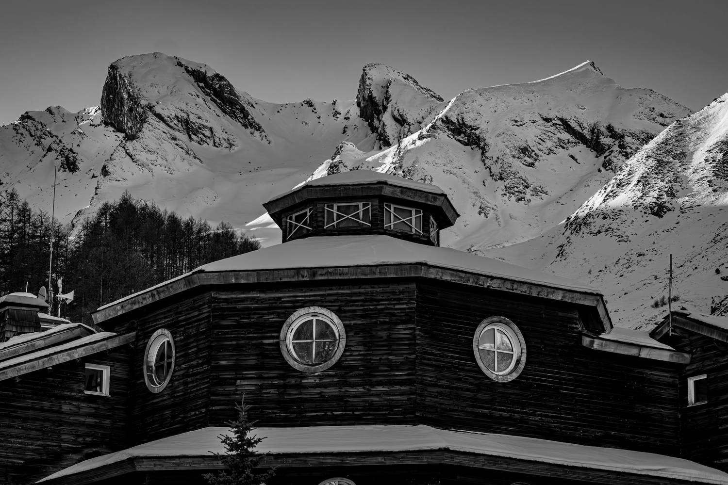A rustic cabin set against majestic snowy mountains in a classic black and white landscape.