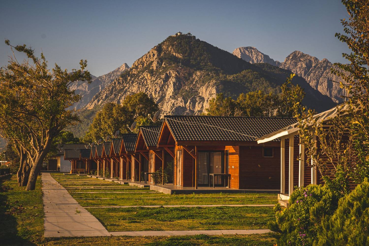 A row of wooden bungalows nestled against a scenic mountain backdrop, surrounded by nature.