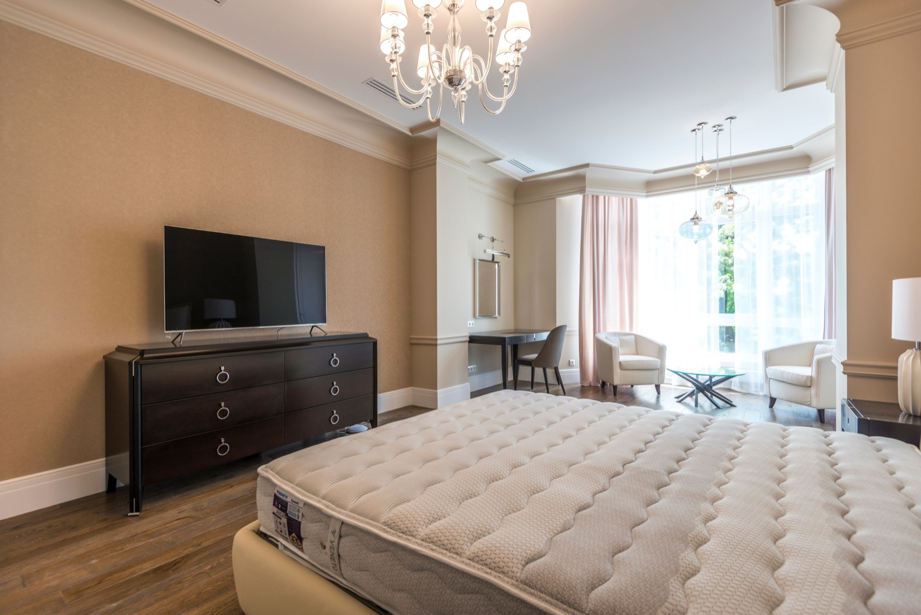 A spacious suite with crown moulding, a chandelier, oak flooring and soft daylight from a bay window
